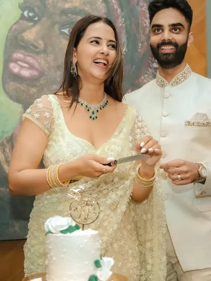 A joyous cake-cutting moment during an indoor engagement celebration in Pune. The couple's happiness is the focus, framed by modern decor and a beautiful piece of art, capturing the celebratory spirit of the occasion.