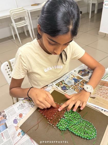 A close-up shot of young hands carefully weaving string around the nails to create a potted cactus design.