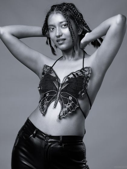 A full-body black and white portrait of a model in a butterfly top and leather pants. The monochrome edit gives this conceptual outfit a timeless, artistic quality.