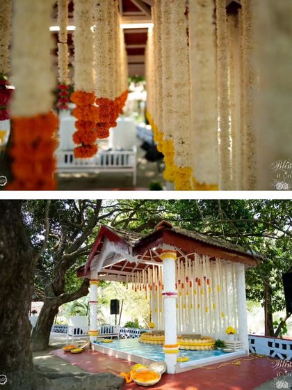 A charming and rustic Haldi ceremony setup in a traditional tiled-roof structure. The space is brightened with hanging garlands of white, yellow, and orange flowers.