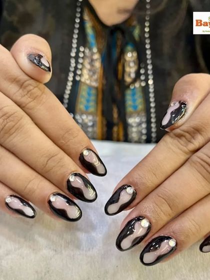 Bold and beautiful nails. This abstract design features a nude base with creative black swirls and a single rhinestone at the cuticle for a modern, artistic look.