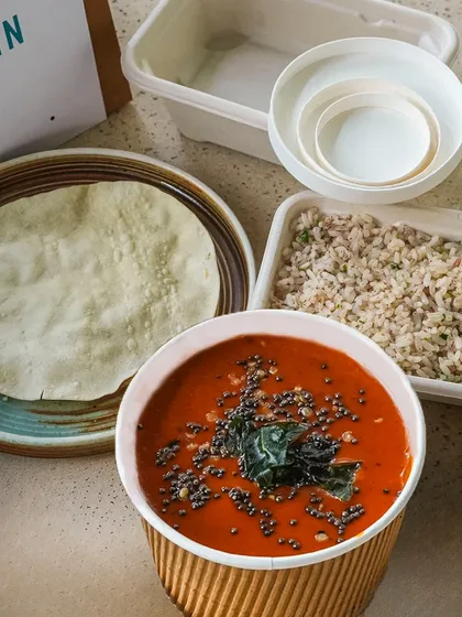 A vibrant curry, packed hot and ready to be poured over rice. The tempered spices on top are a final touch that blooms with aroma when you open the container.