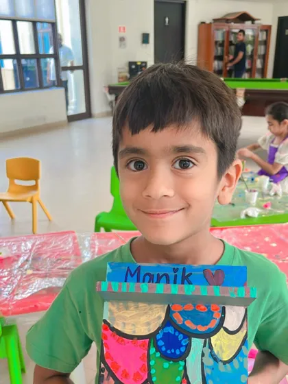 A sweet smile from a student holding the colorful nameplate he made for his dad, Manik.