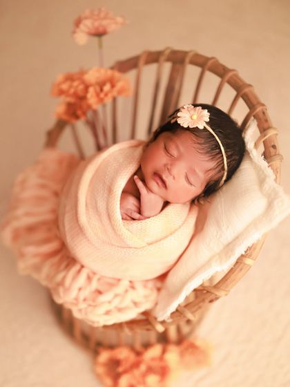 Peach tones are so warm and lovely for newborn portraits. This little girl is nestled in a rattan chair with a matching wrap, headband, and delicate flowers.