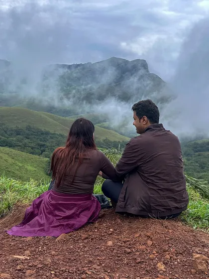 A couple enjoys a quiet moment together, gazing at the misty mountains of Kudremukha. Our treks are perfect for partners who love adventure.