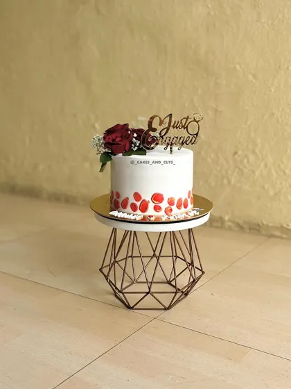 A simple yet elegant single-tier cake for an engagement celebration, decorated with fresh red roses and a beautiful "Just Engaged" topper.