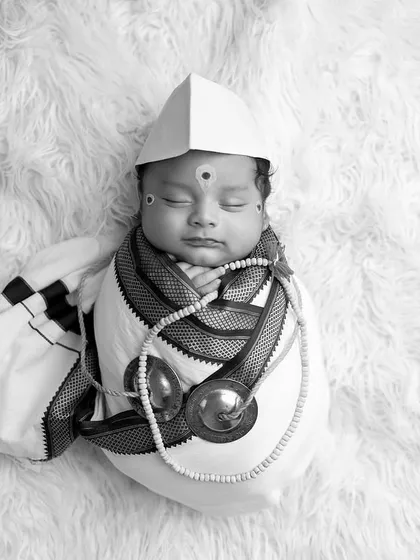 A top-down black and white shot of the baby in Warkari attire, lying on a fluffy white rug, creating a beautiful contrast in textures.