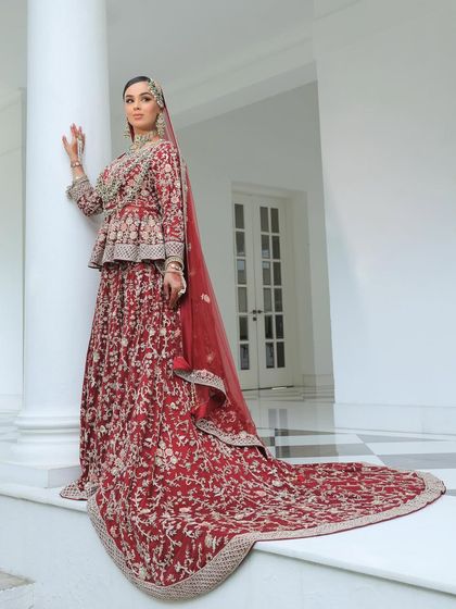 A full-length shot of the Nikkah bride in her magnificent red peplum-style lehenga with a long train. The overall look is one of regal elegance and modern flair.