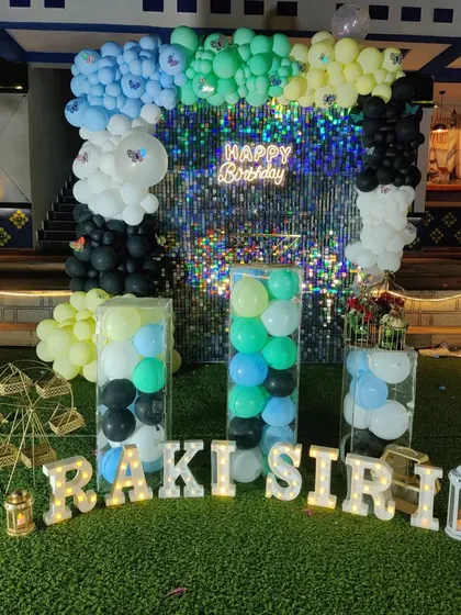 A colorful shimmer wall decoration with a multi-colored balloon arch and transparent plinths filled with balloons.