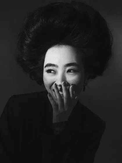 A candid, joyful moment captured during a highly structured, avant-garde hair shoot. This black and white image contrasts the elaborate hairstyle with a genuine, spontaneous expression.
