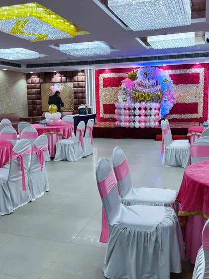 A full banquet hall setup for a 13th birthday, with a balloon stage decoration and matching chair covers.