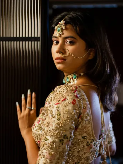 A classic bridal pose looking over the shoulder. This shot beautifully showcases the back of the blouse, the intricate jewelry, and the bride's elegant profile against a modern, textured wall.