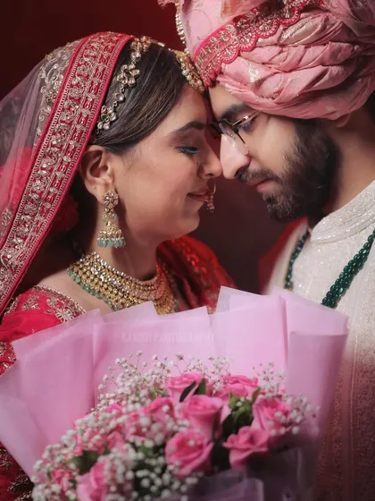 An intimate close-up of a wedding couple, their foreheads touching, holding a bouquet of pink roses.