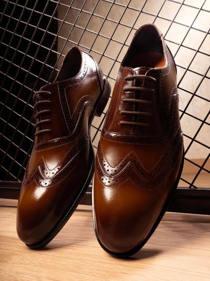 A close-up, heroic shot of the formal leather shoes, focusing on the intricate stitching and rich, polished texture of the leather.