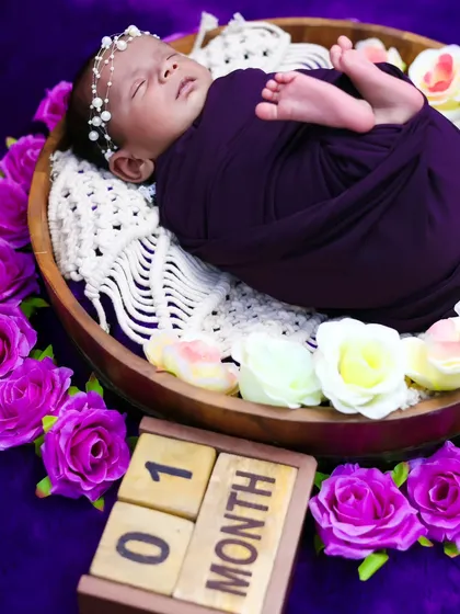 A side view of a one-month-old baby girl in a basket surrounded by flowers, showing the pearl headband and peaceful sleep.