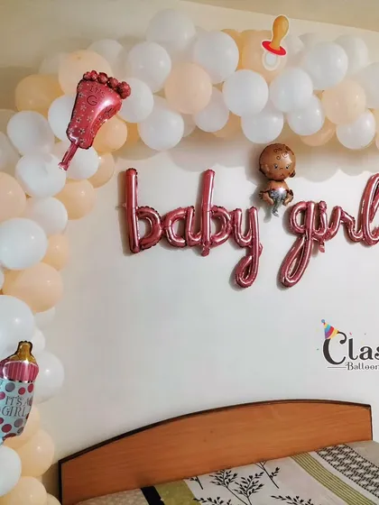 A sweet 'Baby Girl' welcome decoration for over a bed, using a pastel balloon arch and rose gold foil letters.