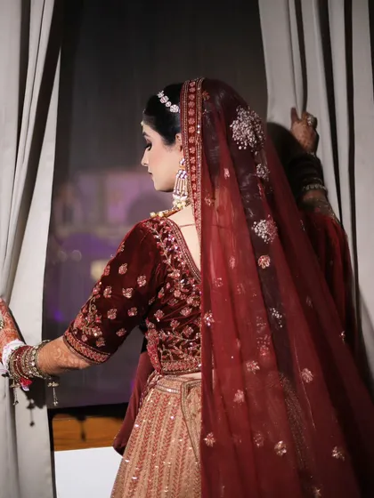 A back shot of the bride in her maroon velvet lehenga, looking out a window. This creates a sense of anticipation and drama.