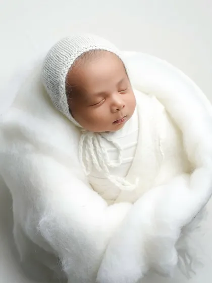 A full-body shot of a newborn nestled in a cloud of soft white fabric. This composition emphasizes how small and precious they are in their first few weeks of life.