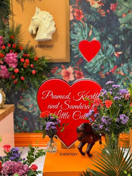 A personalized heart-shaped sign with the parents' names, set amongst lush flowers.