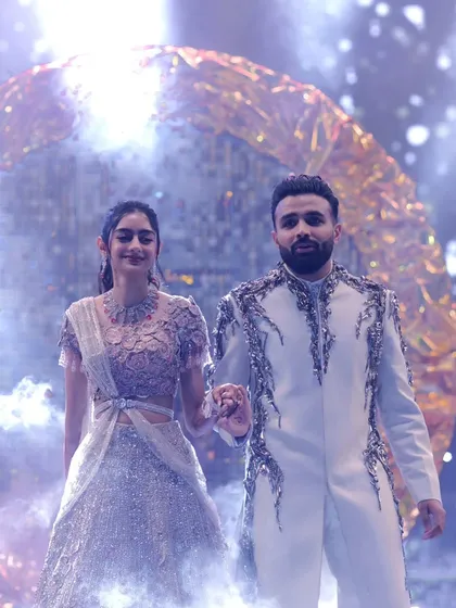 The couple making their grand entrance, hand-in-hand. The combination of a shimmering backdrop and atmospheric smoke creates a magical and dramatic start to their Sangeet night.