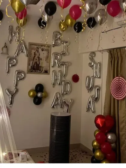 A full view of a romantic birthday room setup, showing the bed canopy, 'Happy Birthday' foil balloons, and decorations covering the entire room.