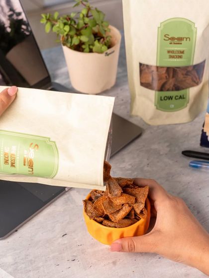 Time for a snack break. A person pours my Nachni Chips from the bag into a bowl at their desk, a simple ritual to pause and snack right.