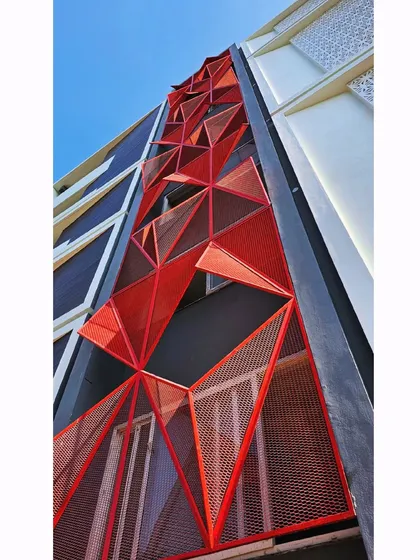 An upward-looking view of the red facade, highlighting the dynamic, three-dimensional quality of the triangular panels against the blue sky.