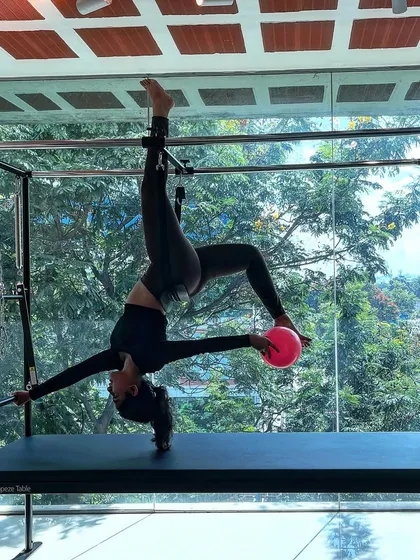 Your presence should brighten the surroundings. This inverted pose on the Cadillac, incorporating the small stability ball, adds a layer of challenge and playfulness.