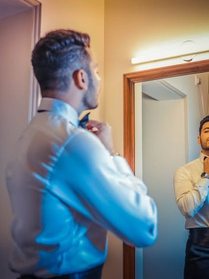 The groom gets ready, adjusting his bow tie in the mirror, a classic getting-ready shot.