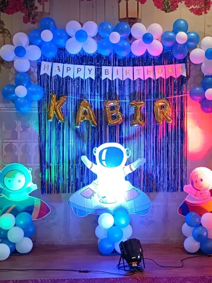 A well-lit view of the space-themed birthday decoration. The combination of foil name balloons, a 'Happy Birthday' banner, and character props creates a complete and exciting look.