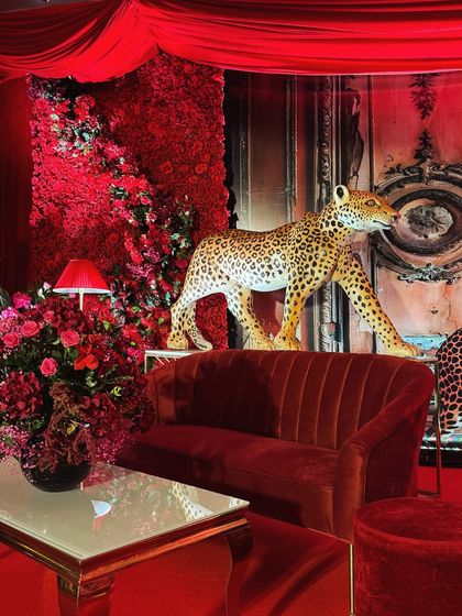 Every detail was chosen to build a narrative. A life-sized leopard figure stands proudly beside a velvet lounge setting, set against a wall of red florals, creating layers of texture and intrigue.
