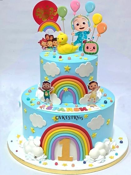 A bright and happy two-tier Cocomelon cake. This design features multiple fondant rainbows, clouds, and all the favorite characters for a joyful first birthday.