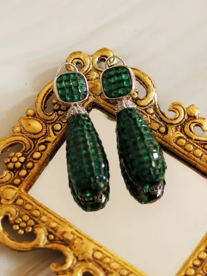 A vintage-inspired golden mirror perfectly frames these emerald green earrings. The reflection adds depth, while the ornate frame complements the jewelry's luxurious and timeless design.