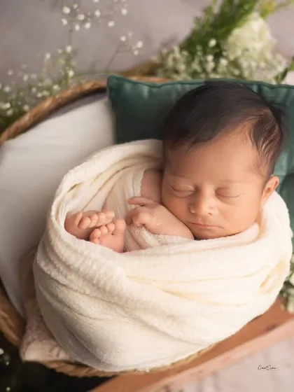Simplicity at its best. This baby is sleeping peacefully in a basket, wrapped in a cream swaddle with just a hint of greenery and a soft pillow for support.