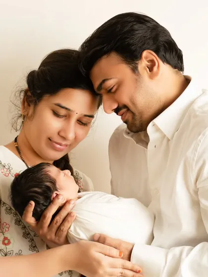 A classic and radiant family portrait with both parents gazing lovingly at their newborn. The clean, bright lighting and simple white outfits create a timeless and pure image of new parenthood.