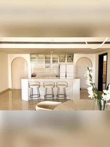 This home features a stunning open-plan kitchen with a fluted bar counter and a custom wine rack. The design uses arches and a clean white palette to create a space that is perfect for entertaining.