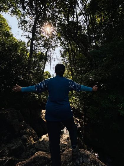 A trekker embracing the forest, with the sun filtering through the trees on the Narasimha Parvatha trail.
