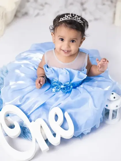This little princess is all smiles for her first birthday portrait. The simple white background and "One" sign keep the focus on her.