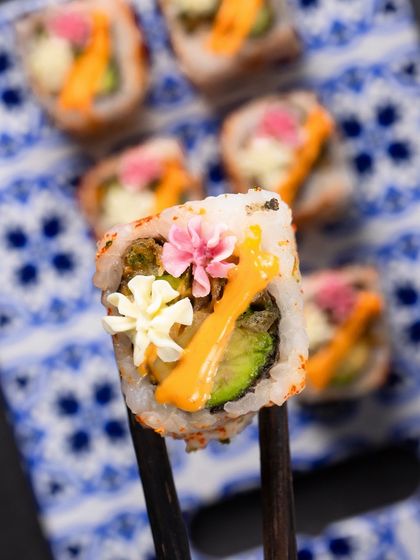 A perfect single bite of the Avocado Asparagus Tempura roll held up by chopsticks.