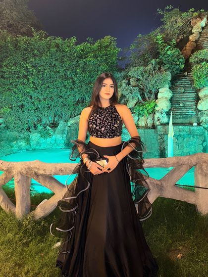 A full-length shot of the custom black lehenga, showing its complete silhouette against a beautiful waterfall backdrop.