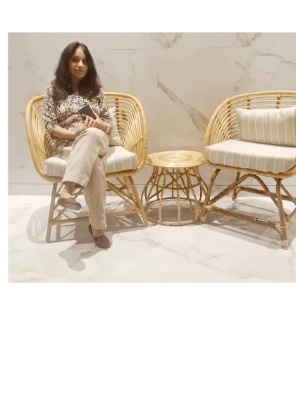 A customer enjoying our handcrafted rattan chair and table set. This image shows the scale and comfort of our furniture in a real-world setting, featuring elegant armchairs with striped cushions and a matching side table.