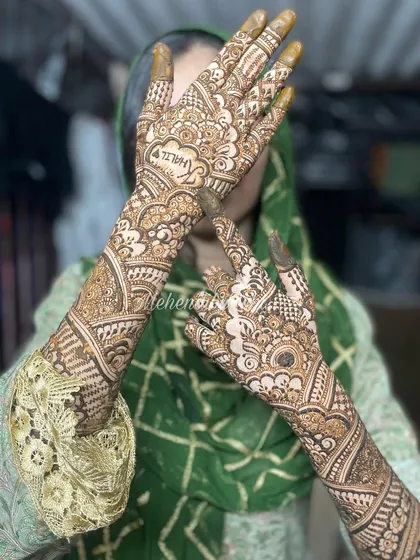 An elegant pose for an engagement mehendi. This design features the groom's name hidden within the intricate patterns that flow from the fingers to the mid-forearm.