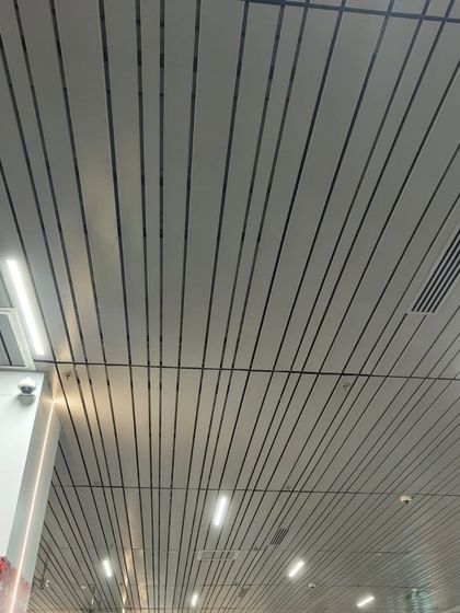 A modern, linear metal ceiling in a commercial space. The sleek white panels with black grooves integrate lighting and air conditioning vents for a clean, minimalist finish.