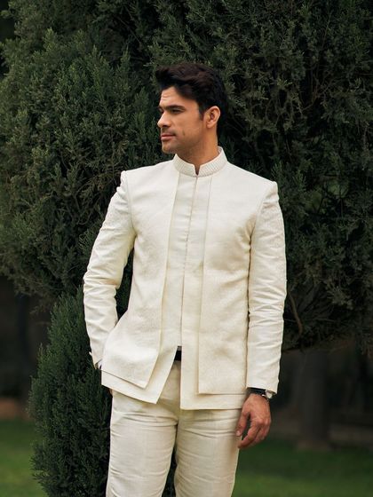 An all-ivory Jodhpuri suit offers a clean, minimalist, and incredibly chic look. The layered front panel adds a unique structural detail to this monochrome ensemble.