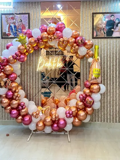 A trendy circular ring stand decorated with a lush garland of rose gold, magenta, and white balloons for a 'Bride to be' party, featuring a central neon sign.