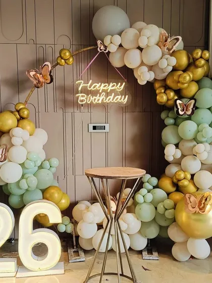 A chic and modern birthday setup for a 26th birthday. The circular balloon arch in sage green, white, and gold, along with the neon sign, is perfect for an elegant party.