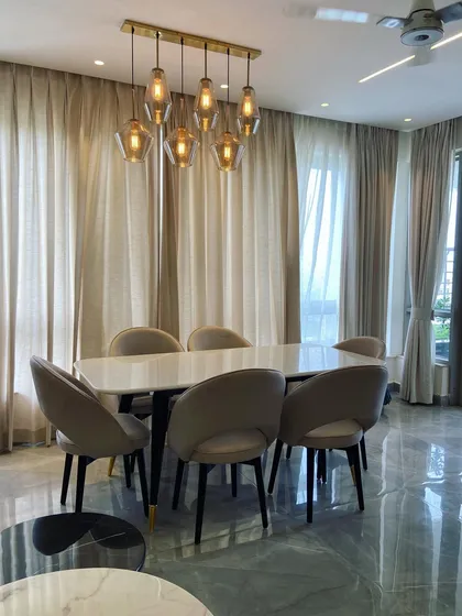 A well-lit dining area from a project in Jaypee Greens, Noida. The design features a marble-top table, comfortable upholstered chairs, and a contemporary cluster of pendant lights that act as a centerpiece, providing both function and style.