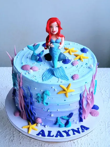 A mermaid-themed cake with an underwater scene created with buttercream textures and fondant details. The hand-sculpted mermaid topper is the star of the show.