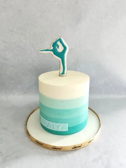 A simple and elegant ballerina-themed cake. The ombre teal buttercream is topped with a custom cookie showing a graceful ballet pose.