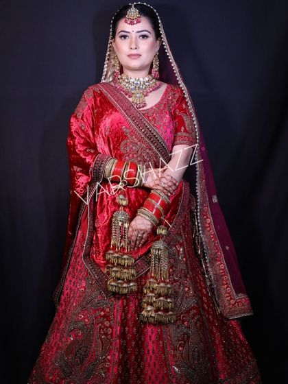 A confident pose from a bride in a red velvet lehenga, showing the full outfit and jewellery set. This look is available for both rent and purchase.